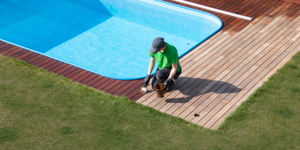 야외 수영장의 목재 바닥에 보호제 칠하는 사람 사진